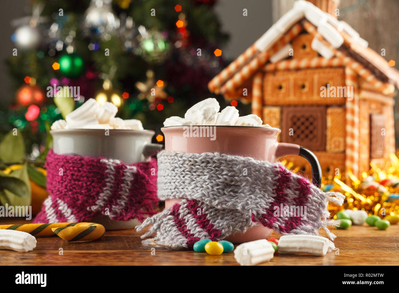 Becher in Schals mit einem heißen Getränk Marshmallows und Süßigkeiten auf dem Hintergrund einer Lebkuchenhaus. Festliche noch leben. Close-up. Stockfoto