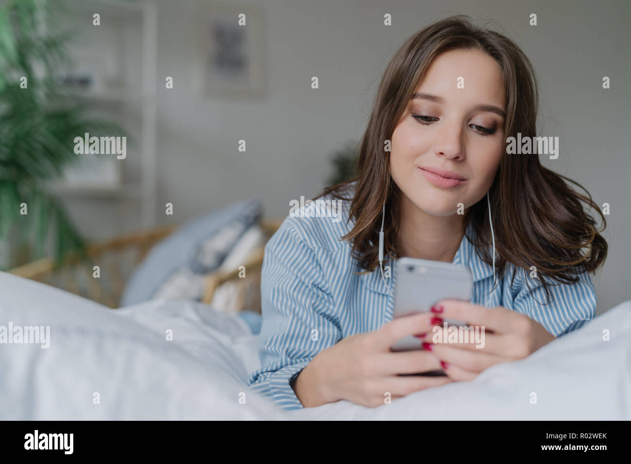 Innen- schuss von attraktiven nachdenkliche junge Frau liegt im Bett, nutzt  moderne Handy, Uhren Video oder Film online, genießt, guter Sound, in pyja  gekleidet Stockfotografie - Alamy