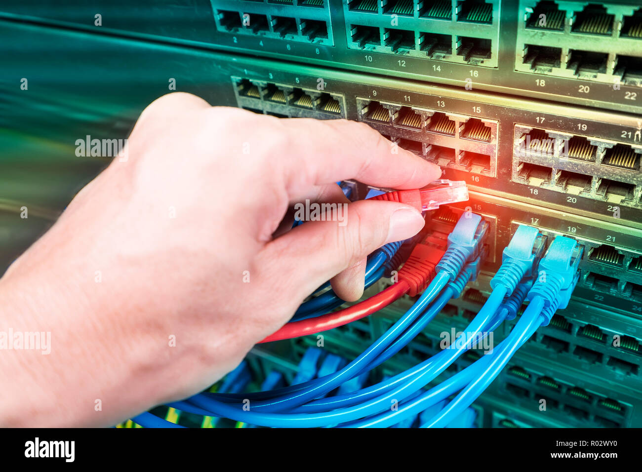 Hand, die Netzwerkkabel auf dem Switch Hub im Server raum Hintergrund Stockfoto