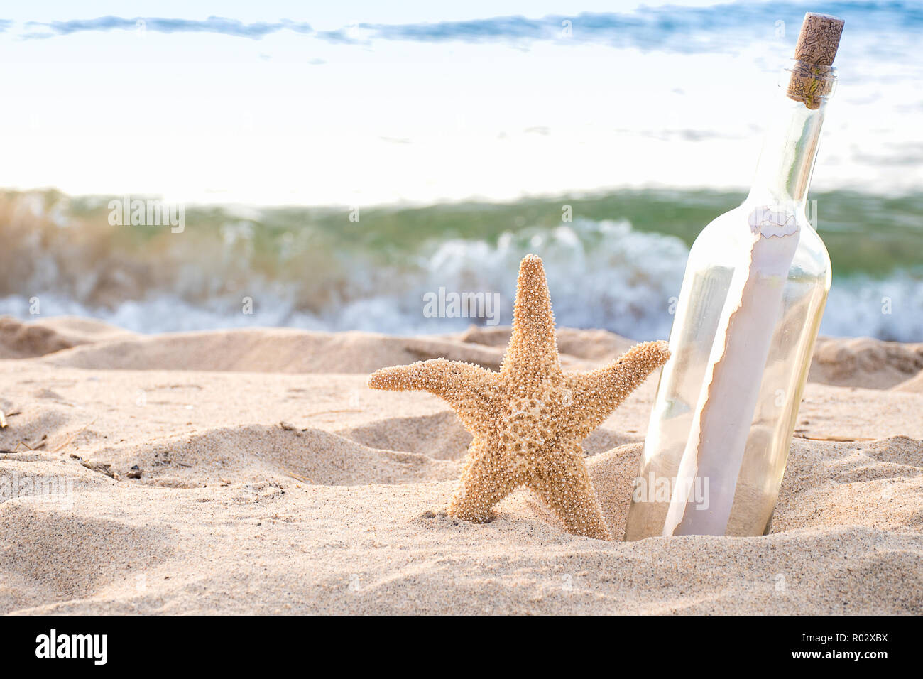 Flaschenpost und Seesterne in Strand Sand mit Ocean Wave Hintergrund Stockfoto