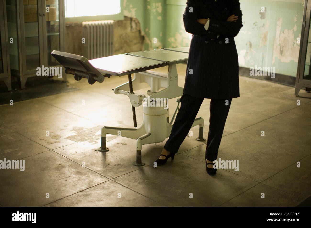Verschränkte Arme eines mittleren nach Business Frau neben einem alten Betriebssystem Tabelle in ein verfallenes Gebäude. Stockfoto