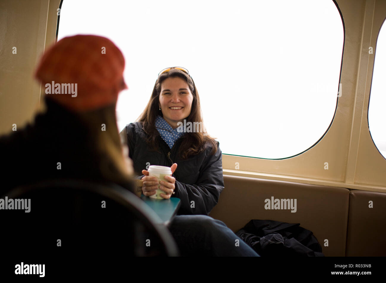 Junge Frau sitzt im Ferry mit Freundin Kaffee trinken und lachen Stockfoto