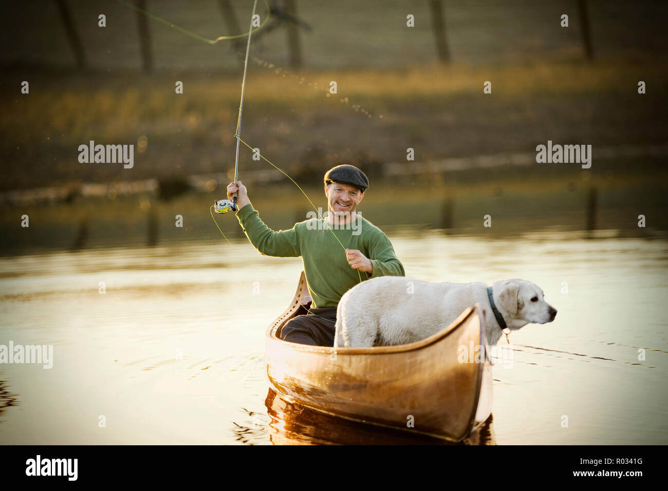 Jungen Erwachsenen Mann mit seinem Hund in einem Kanu angeln an einem See. Stockfoto