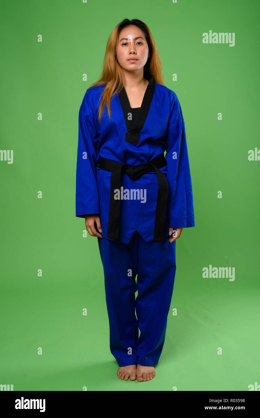 Junge asiatische Frau trägt blaue Karate Gi gegen grüne backgroun Stockfoto