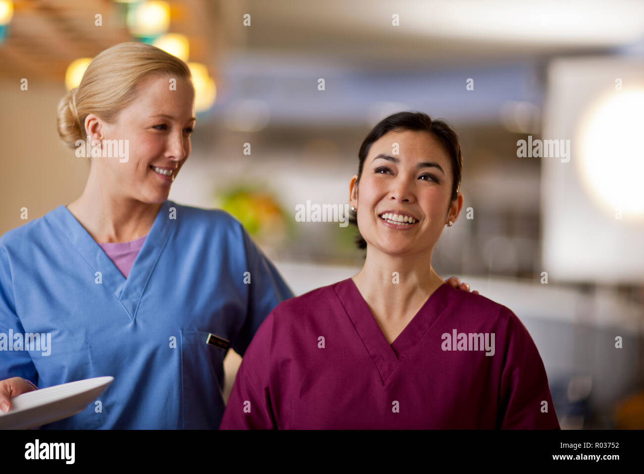Lächelnde junge Krankenschwestern legt ihren Arm um ihre Kollegin wie sie in Linie warten Ihr Mittagessen aus dem Krankenhaus Kantine zu erhalten. Stockfoto