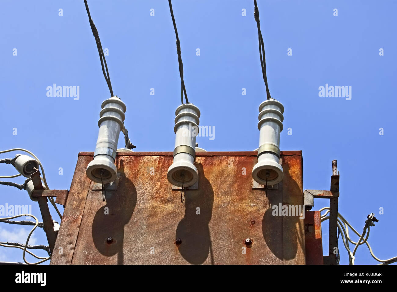 Elektrische Isolatoren und Leitungen auf dem alten 3-phasen Trafo auf dem Hintergrund des blauen Himmels Stockfoto
