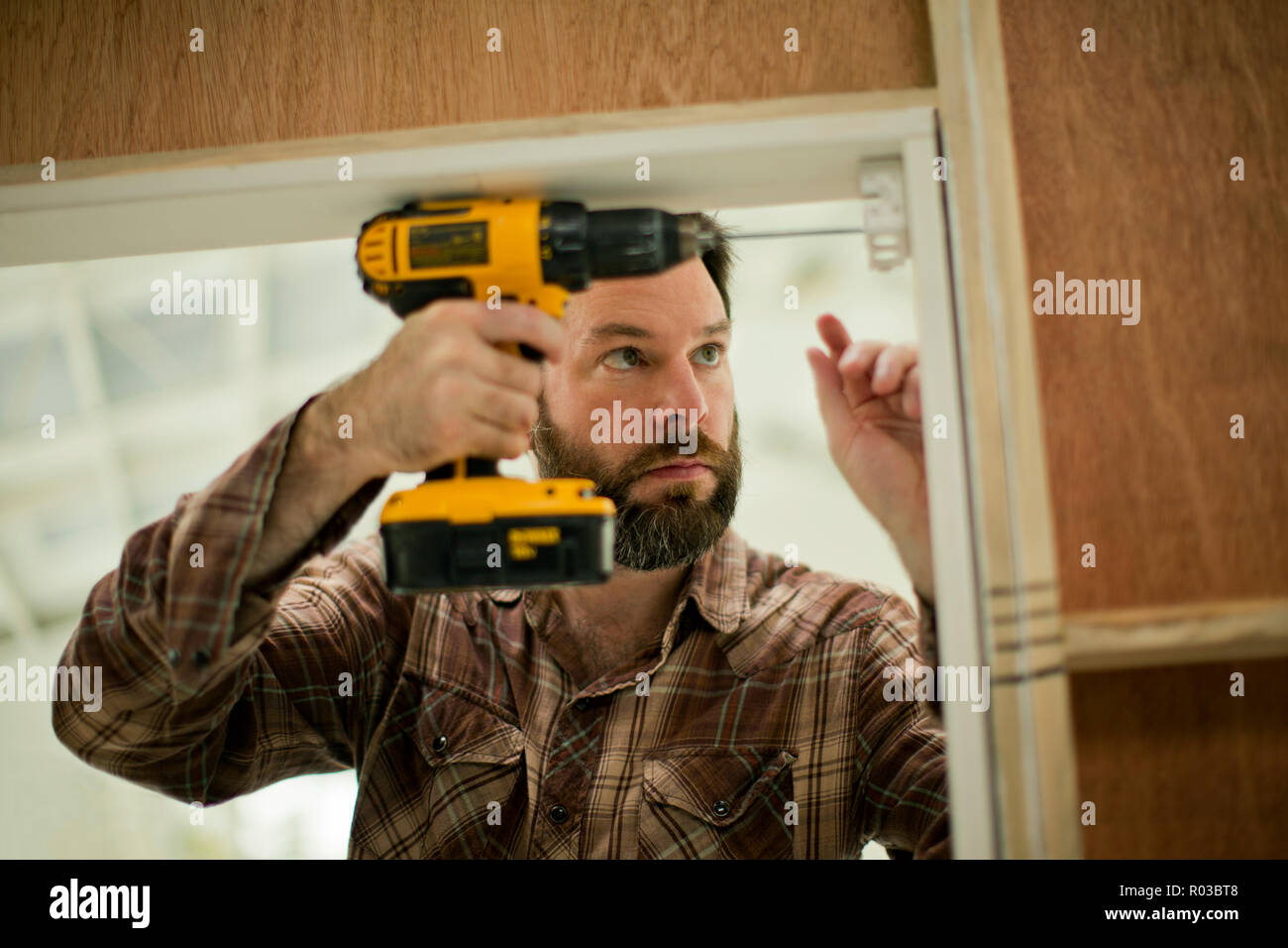 Mitte der erwachsene Mann konzentrieren, als er eine elektrische Bohrmaschine hält, während das Ausbessern der Türrahmen. Stockfoto