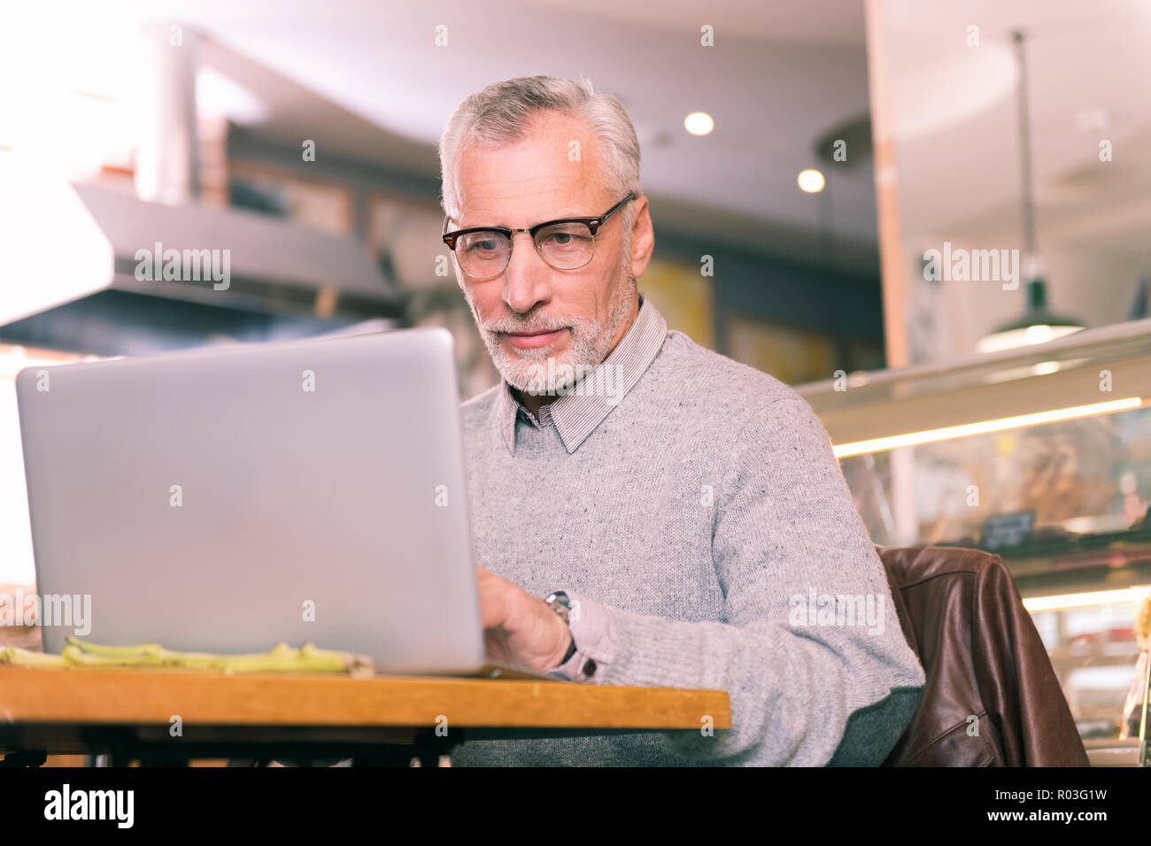 Stattliche reifer Mann mit grauen pullover arbeiten hart daran, mit seinem Laptop Stockfoto