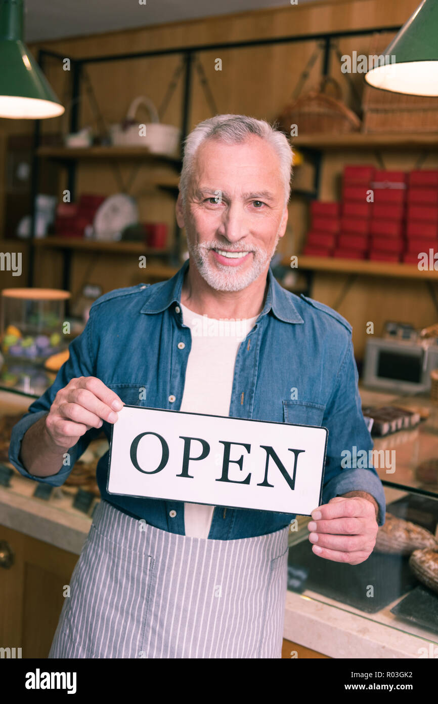 Lächelnde grauhaarige Geschäftsmann tragen Jeanshemd seine Cafeteria öffnen Stockfoto