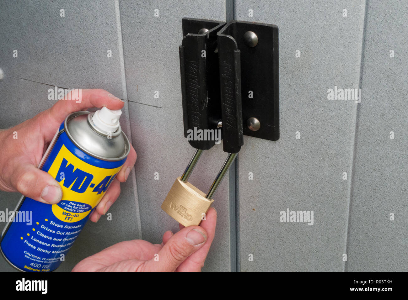 Kaukasische Mann Spritzen einer Aerosoldose WD-40 Schmiermittel auf ein Metall Vorhängeschloss, Großbritannien Stockfoto