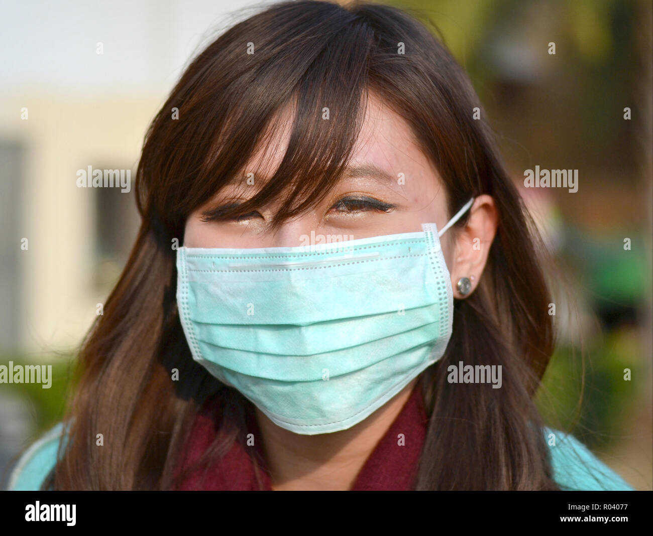 Junge Taiwanese Frau mit orientalischen Augen trägt ein hell-grün Einmal-OP-ohrläppchen Gesichtsmaske. Stockfoto