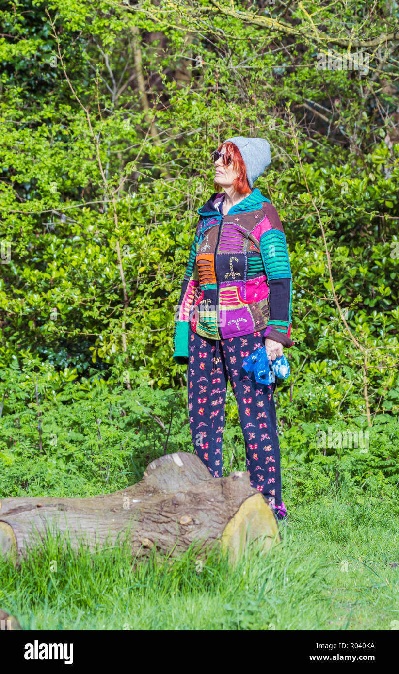 Ältere Frau, die im Wald und schaut lächelnd, tragen cool aussehende jüngere Personen bunte Kleidung. Stockfoto