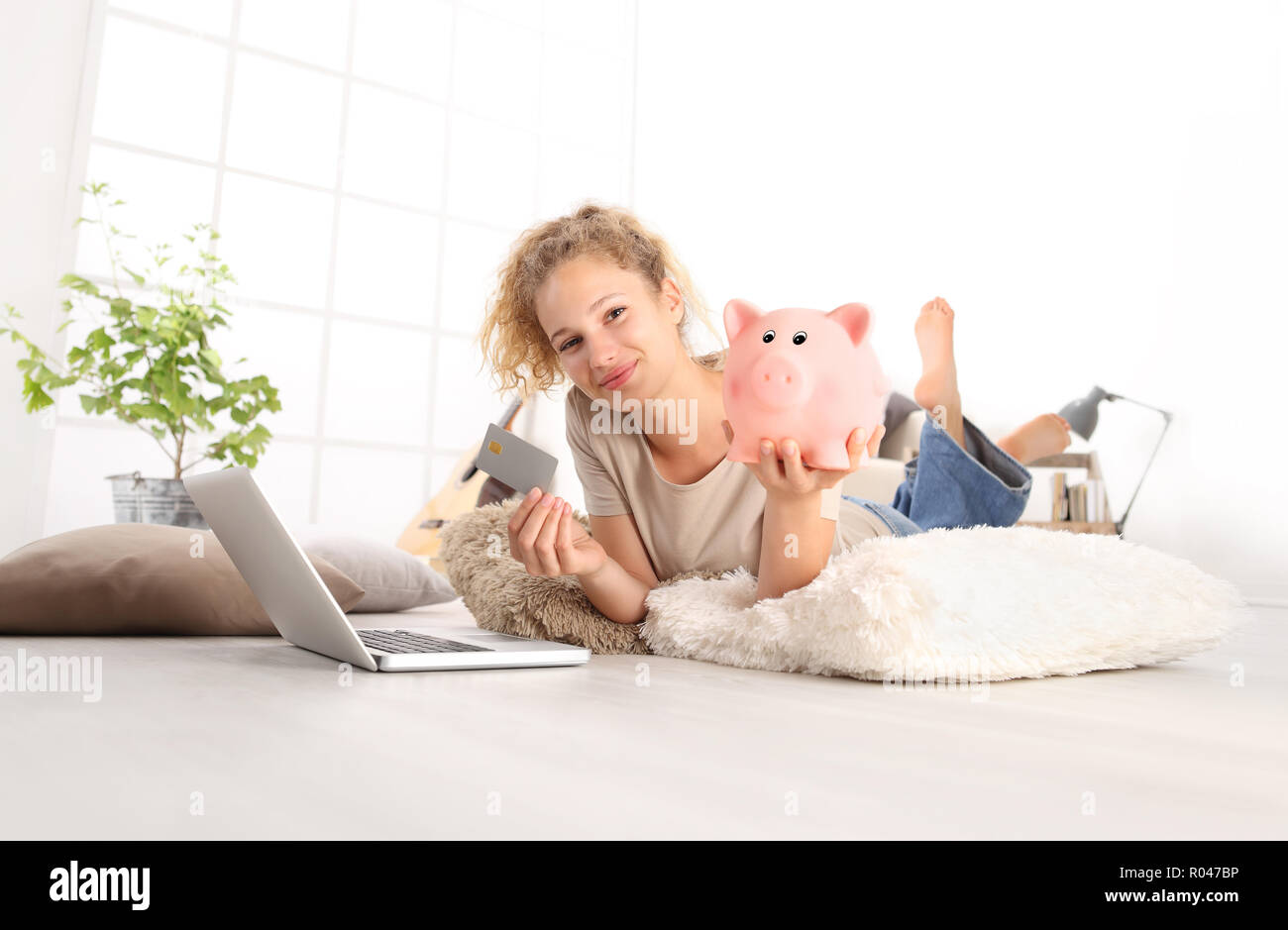 Junge Frau mit Kreditkarte und Sparschwein mit Laptop Computer. Online shopping Konzept speichern, Liegen auf Wohnzimmer Holzboden in modernen whit Stockfoto