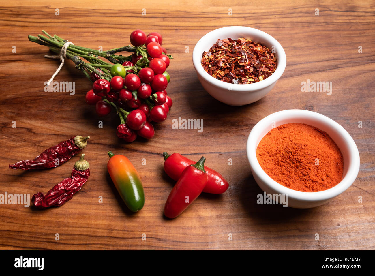 Gruppe von frischen und trockenen Peperoni mit Chilipulver und crushed Red Hot peppers auf einem rustikalen Holzmöbeln Hintergrund. Stockfoto