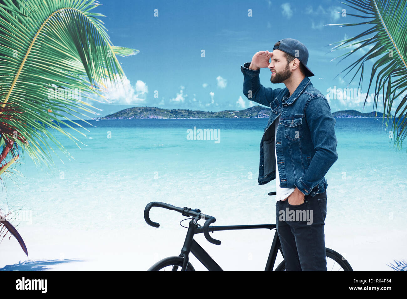 Urlaub am Strand. Junge stilvollen Mann stand am Strand mit Fahrrad vorwärts schauen aufgeregt Stockfoto