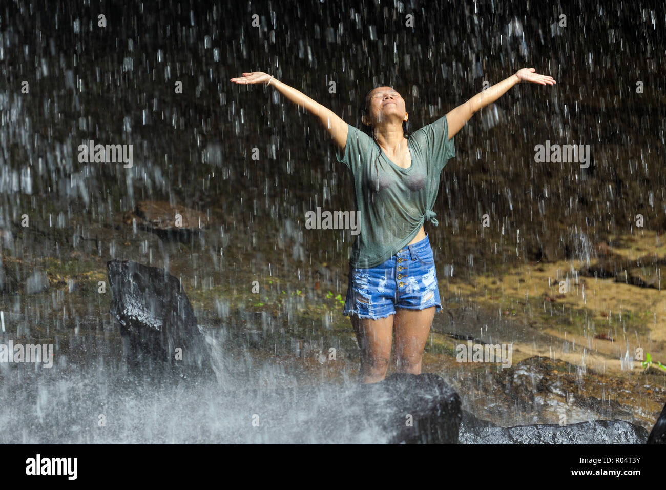 Happy gekleidete Frau ihre Arme überdehnung unter tropischen Wasserfall, Thailand Stockfoto