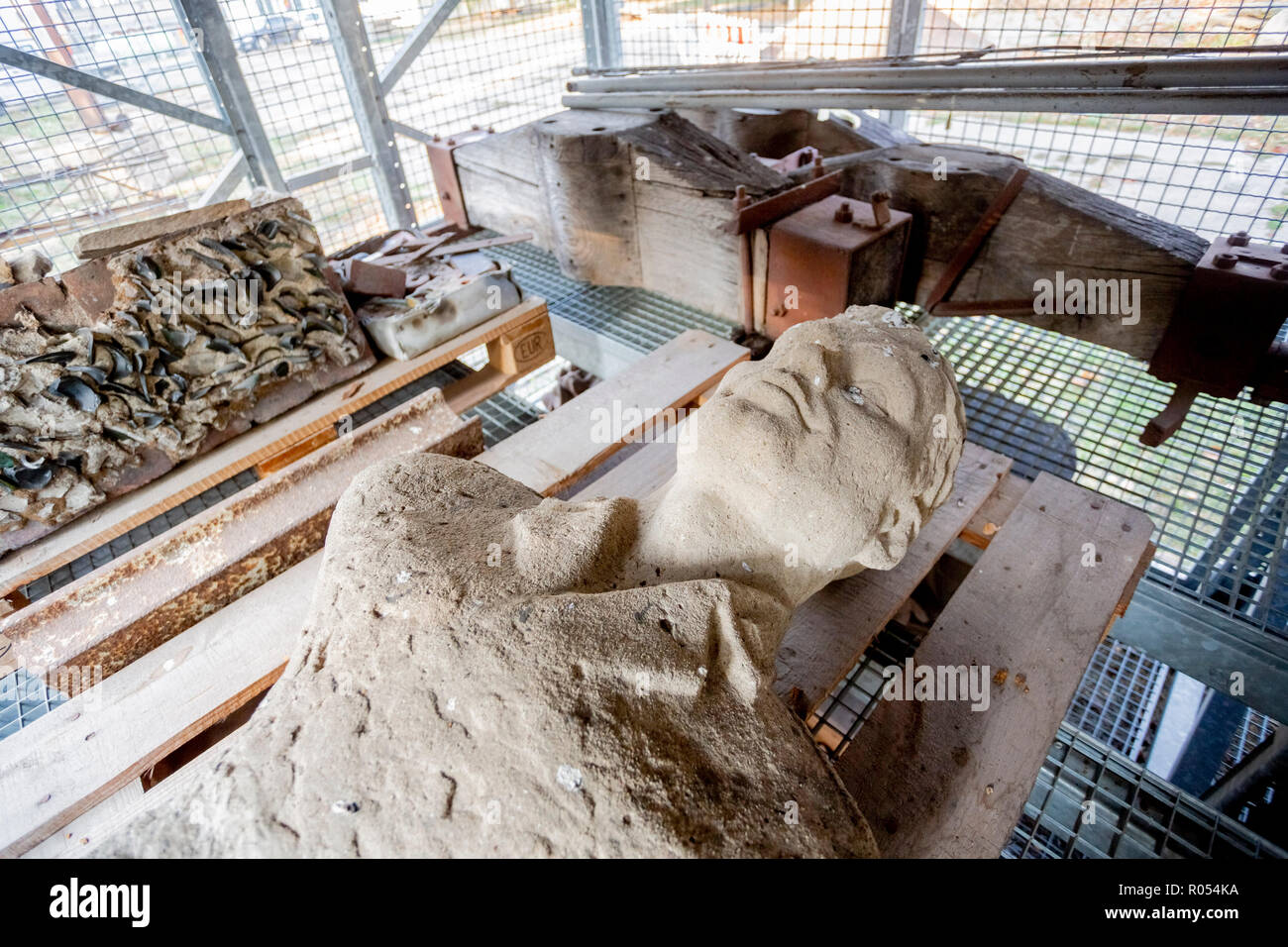 18 Oktober 2018, Berlin: Die Büste der DDR-Grenzsoldaten Egon Schultz, der versehentlich durch einen anderen DDR-Grenzsoldaten war im Tunnel 57 bei einem Austausch des Feuers mit Escape Helfer schossen, liegt auf einem Regal im Lapidarium der Berliner Mauer Stiftung. Dahinter liegt die Träger des Glockenläuten der Kirche der Versöhnung und links davon ein Stück der Friedhofsmauer des Sophien Gemeinde, die als Grenzmauer serviert. Teile der Wände und in andere Teile der DDR-Grenzanlagen sind im Lapidarium aufbewahrt. (Dpa-KORR" Stacheldraht und Stein Büste - Berlin sammeln Stockfoto