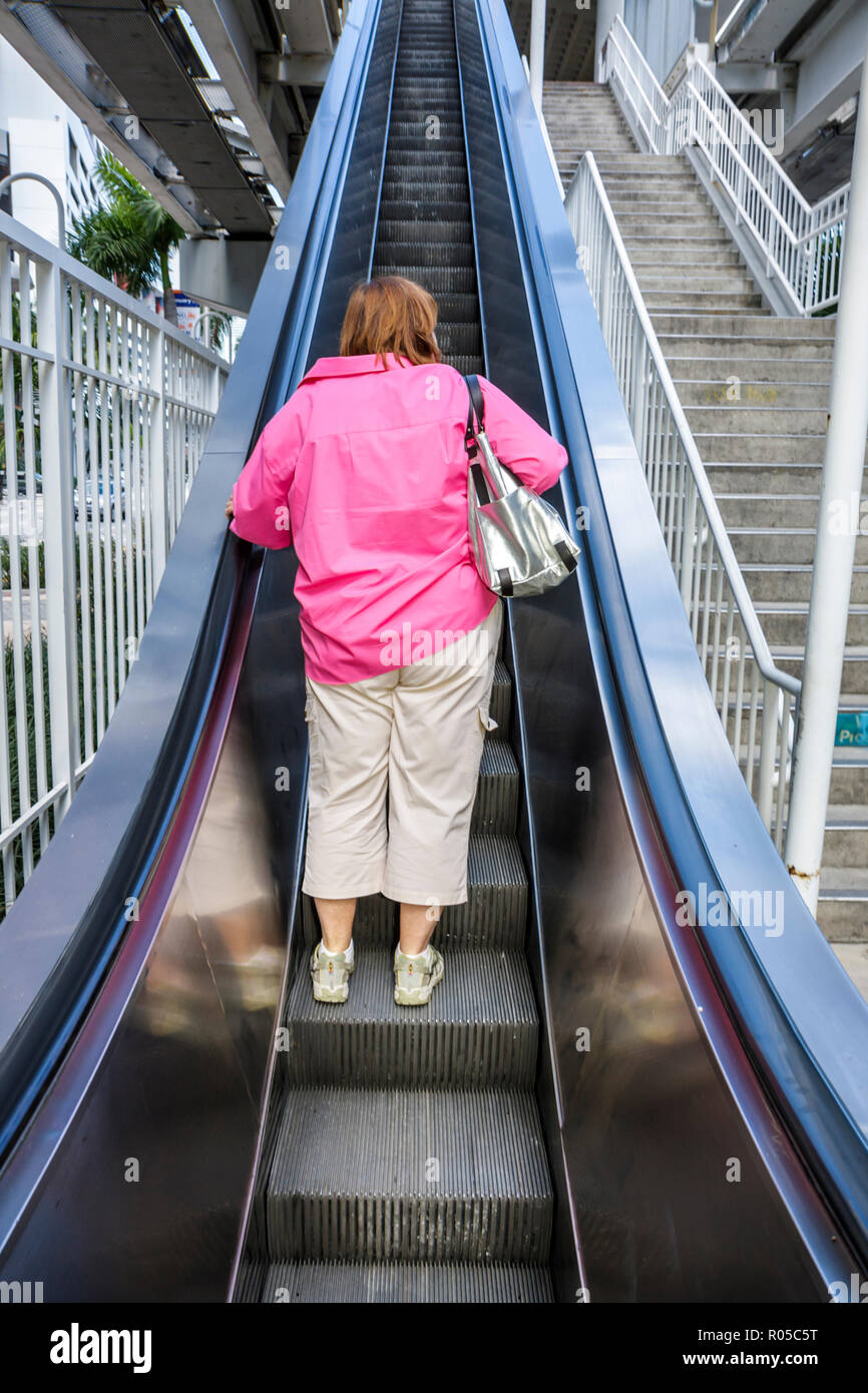 Miami Florida, Innenstadt, Metromover, People Mover Station, Rolltreppe, oben, Aufstieg, Frau weibliche Frauen, hinten, rosa Hemd, große silberne Handtasche Taschenbuch, FL Stockfoto