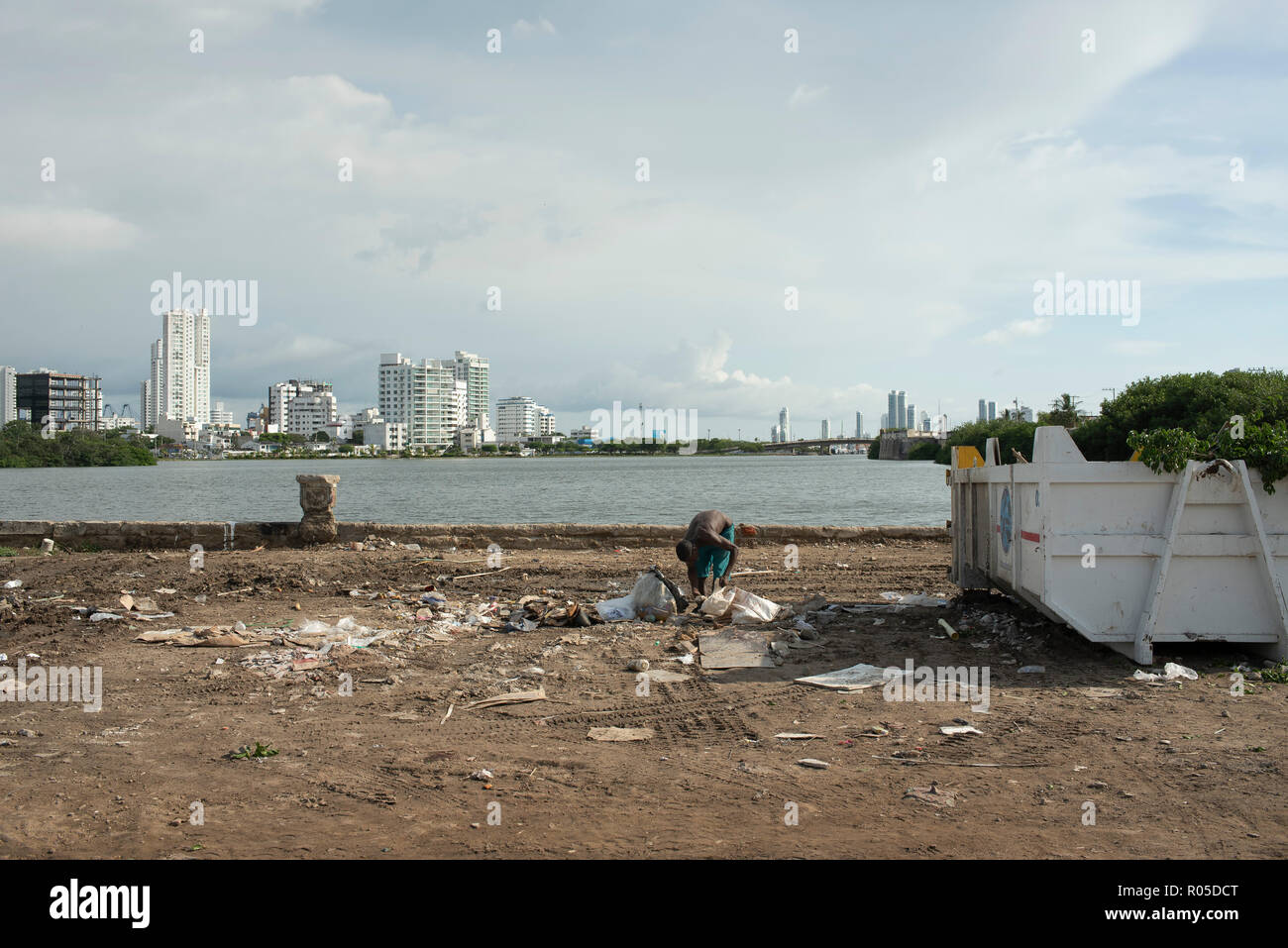 Gegenüberstellung von Arm und Reich. Junge afrikanische Mann sucht durch Müll mit glänzenden neuen Gebäude im Hintergrund. Cartagena, Kolumbien. Sep 2018 Stockfoto
