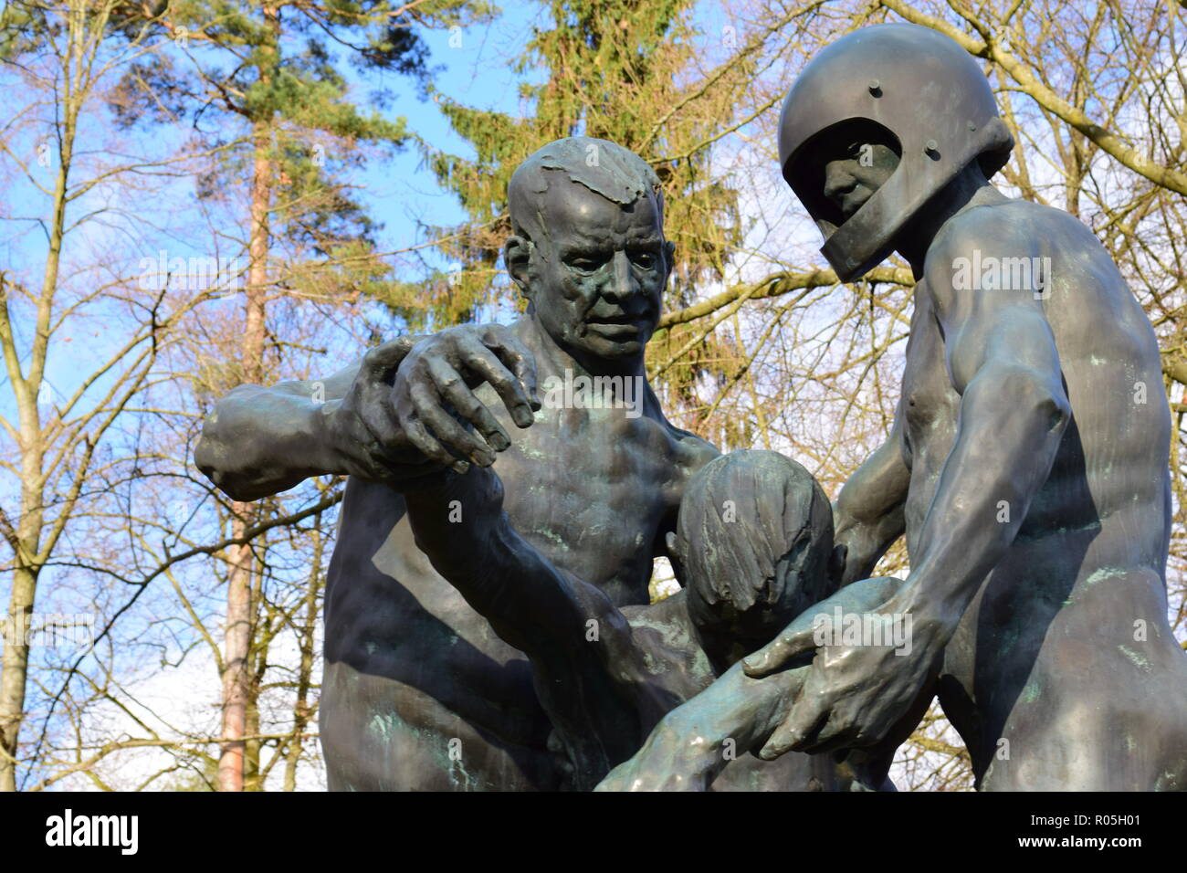 Eine Bronzestatue unter blauem Himmel im Winter in einem Krieg Friedhof zeigt zwei Männer, die ein tödlich verletzte Opfer als ein Symbol der Hilflosigkeit. Stockfoto