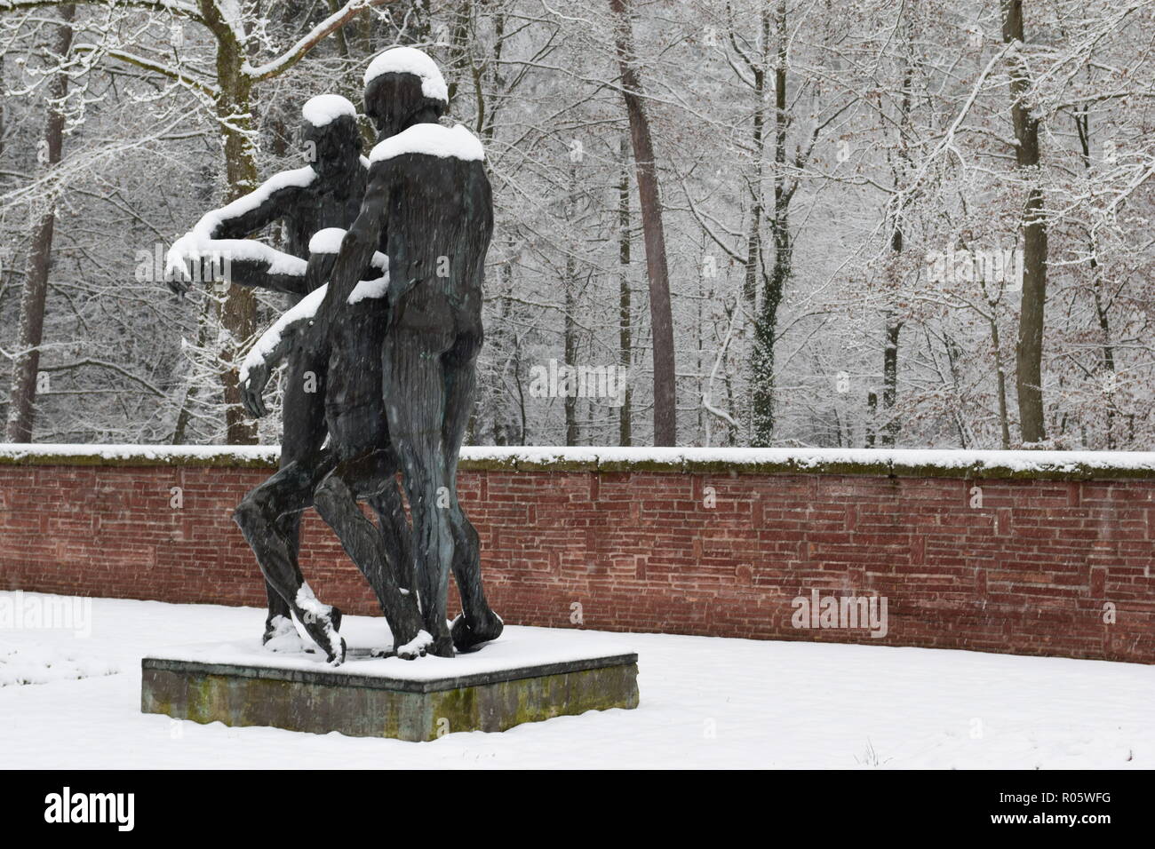 Eine Bronzestatue im Schnee am Soldatenfriedhof in Reimsbach abgedeckt zeigt zwei Männer, die ein tödliches Opfer als Symbol für die Hilflosigkeit der Menschen. Stockfoto