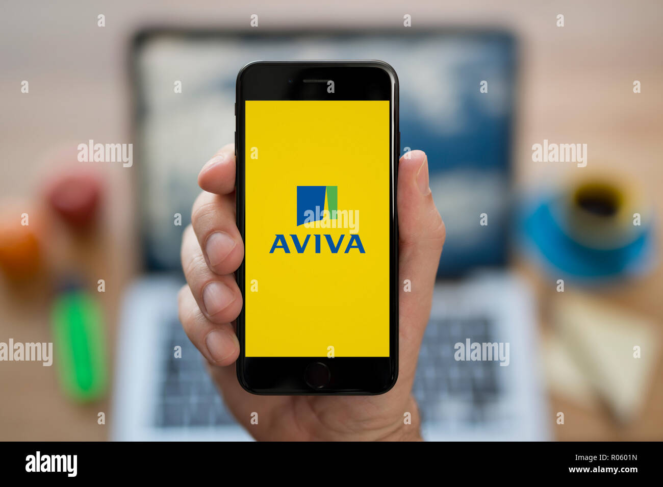 Ein Mann schaut auf seinem iPhone die zeigt die Aviva-Logo, während saß an seinem Computer Schreibtisch (nur redaktionelle Nutzung). Stockfoto