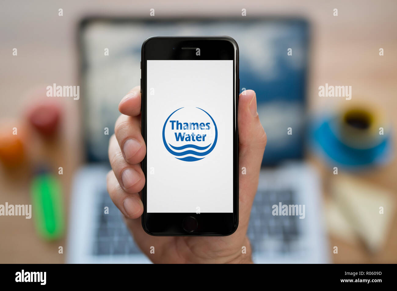 Ein Mann schaut auf seinem iPhone die zeigt die Thames Water logo, während saß an seinem Computer Schreibtisch (nur redaktionelle Nutzung). Stockfoto