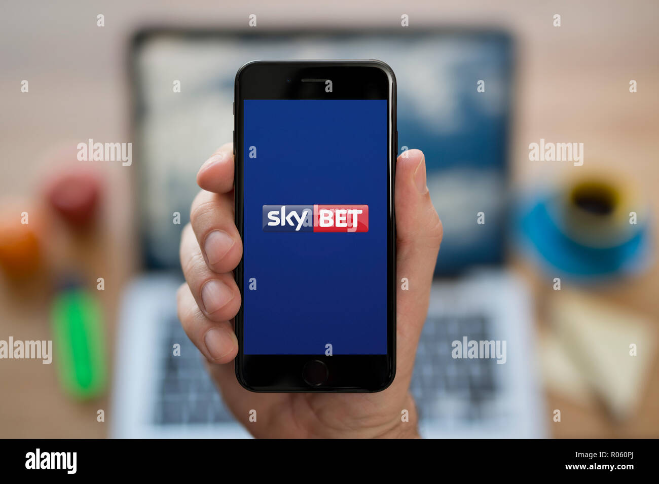 Ein Mann schaut auf seinem iPhone. Das Sky Bet-Logo, während saß an seinem Computer Schreibtisch (nur redaktionelle Nutzung). Stockfoto
