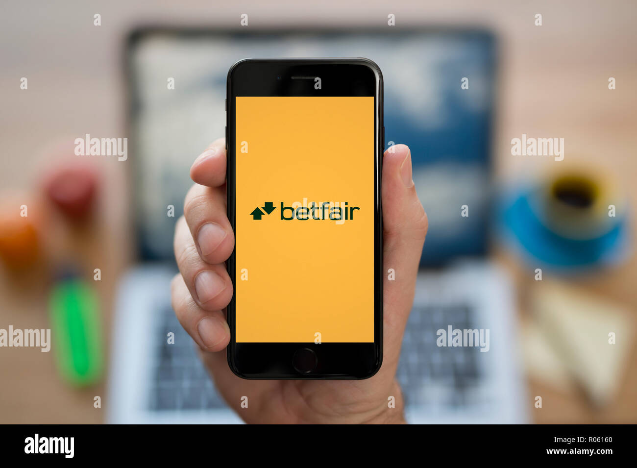 Ein Mann schaut auf seinem iPhone die zeigt die Betfair logo, während saß an seinem Computer Schreibtisch (nur redaktionelle Nutzung). Stockfoto