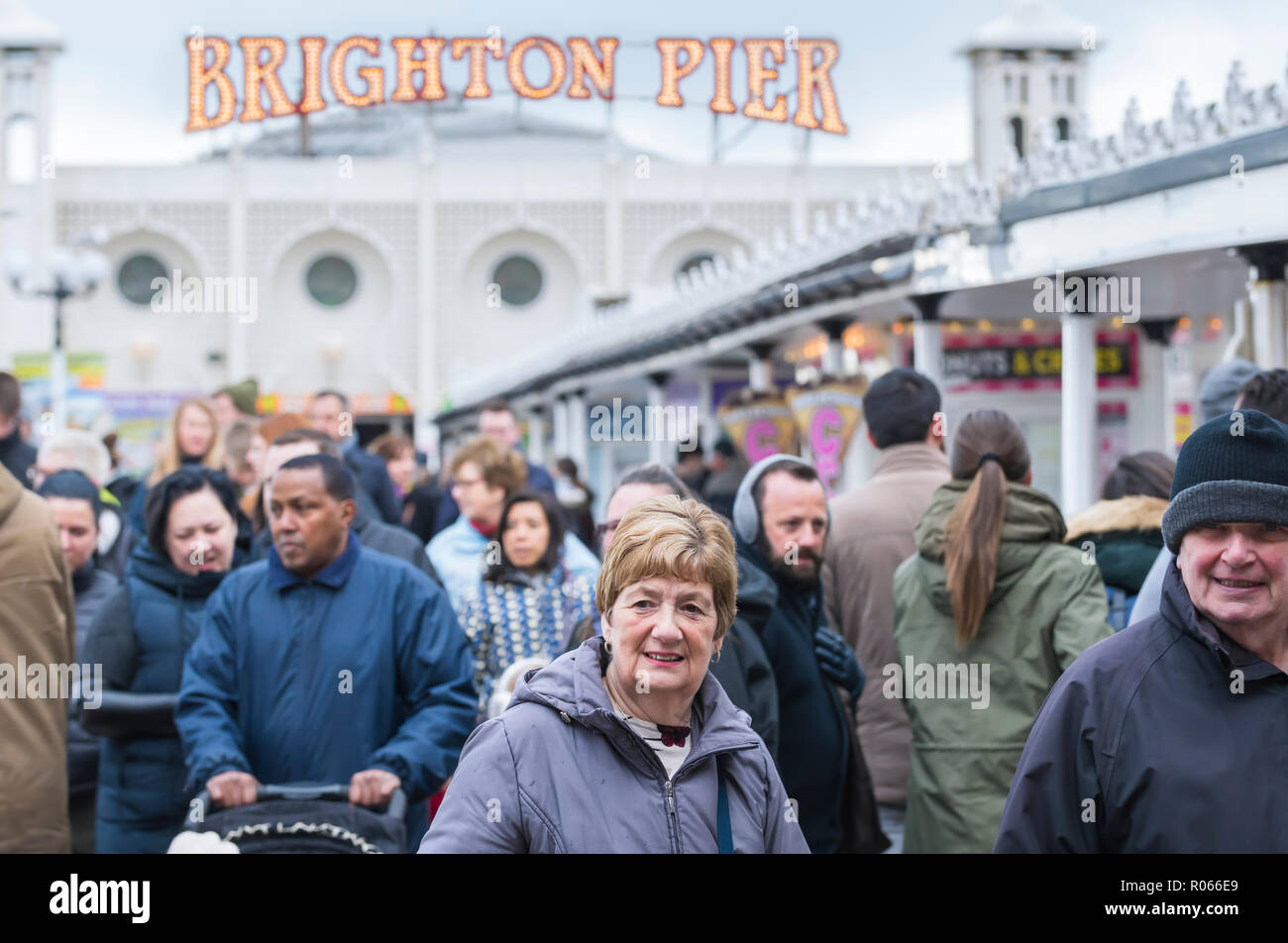 Massen von Menschen Mäntel tragen an einem kalten Tag im Frühling auf einem langen Pier von Brighton, East Sussex, England, UK. Stockfoto