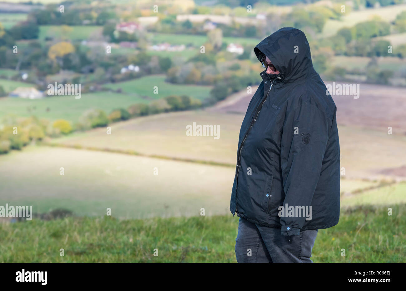 Die Frau trug einen Mantel mit Kapuze bis zu Fuß an einem sehr kalten Tag im Herbst auf der South Downs Hügeln in East Sussex, England, UK. Stockfoto