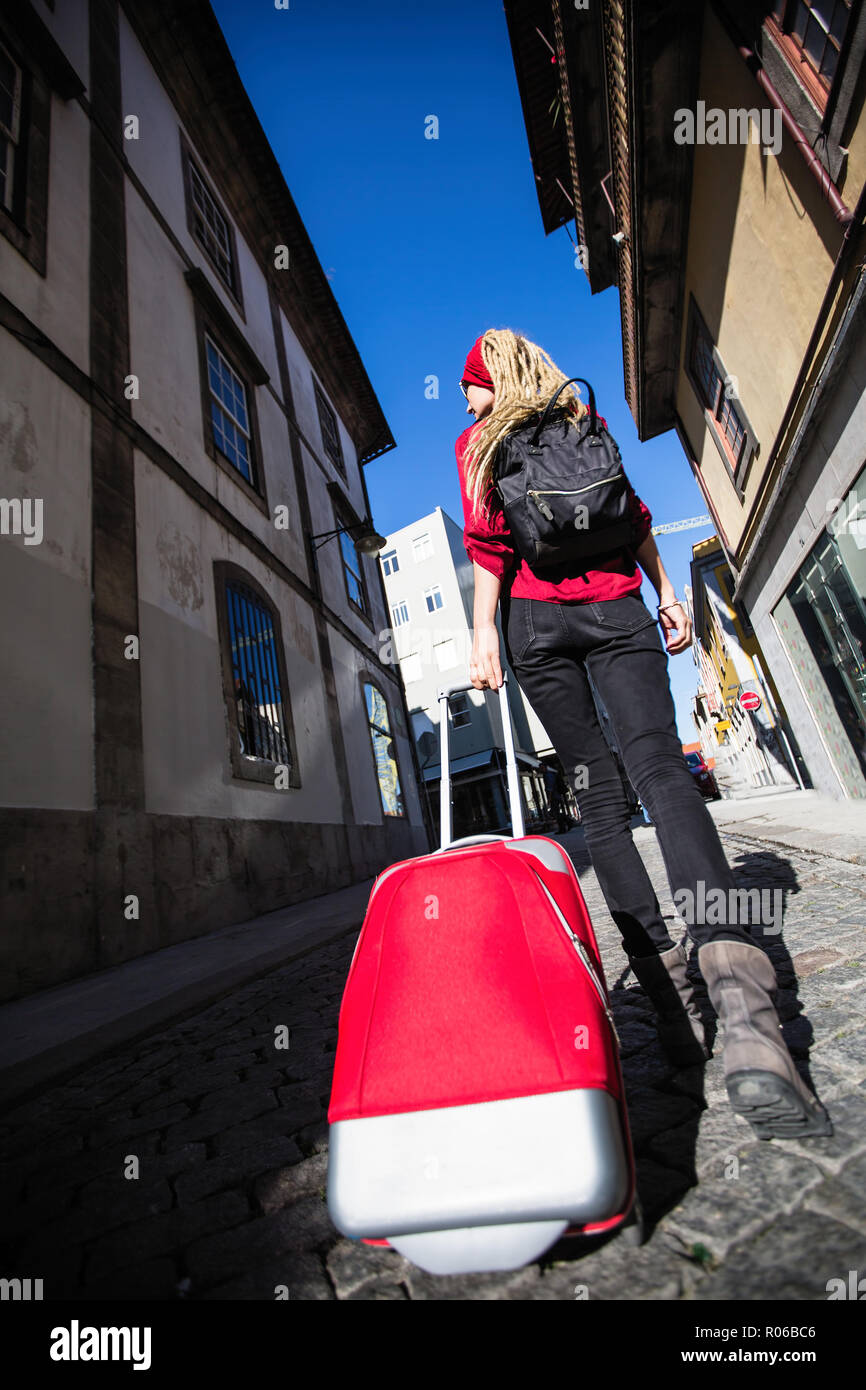 Rückansicht der Frau auf dem Bürgersteig mit einem roten Koffer. Reise und Tourismus. Stockfoto