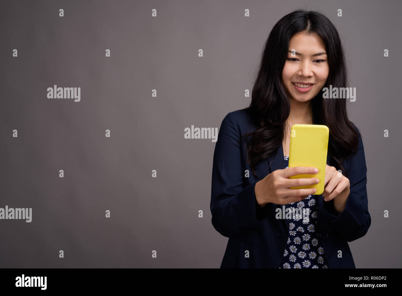 Asiatische Frau mit Handy vor grauem Hintergrund Stockfoto