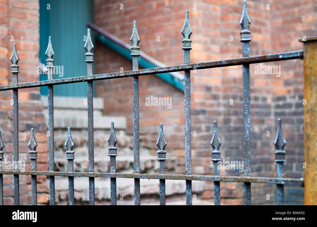 Antiken Schmiedeeisernen Zaun mit selektiven Fokus. Wand mit Tür und Treppe im Hintergrund. Stockfoto