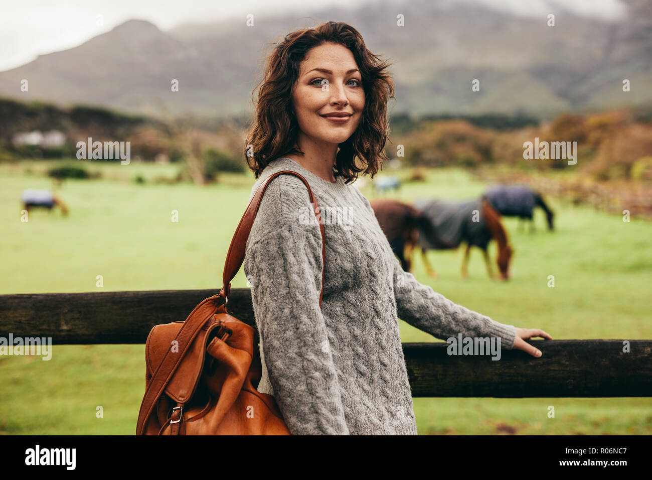 Schöne junge Frau, die in der Landschaft. Frau, die von einem Zaun einer Ranch. Stockfoto