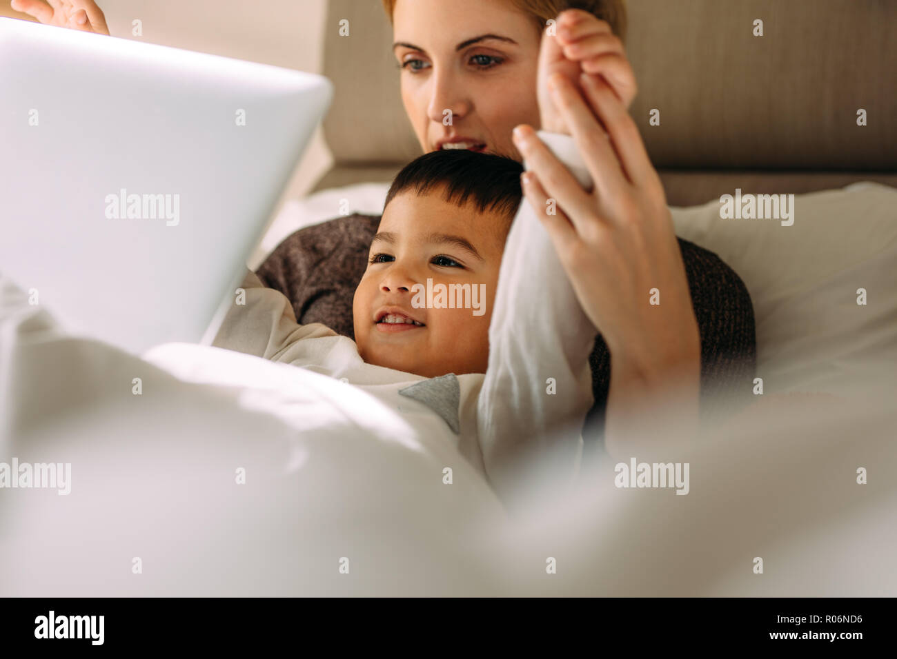 Kleine Junge mit Mutter genießen Sie Cartoon Movie auf Laptop im Bett lag. Junge Frau mit ihrem Sohn auf Laptop mit erhobenen Händen. Stockfoto
