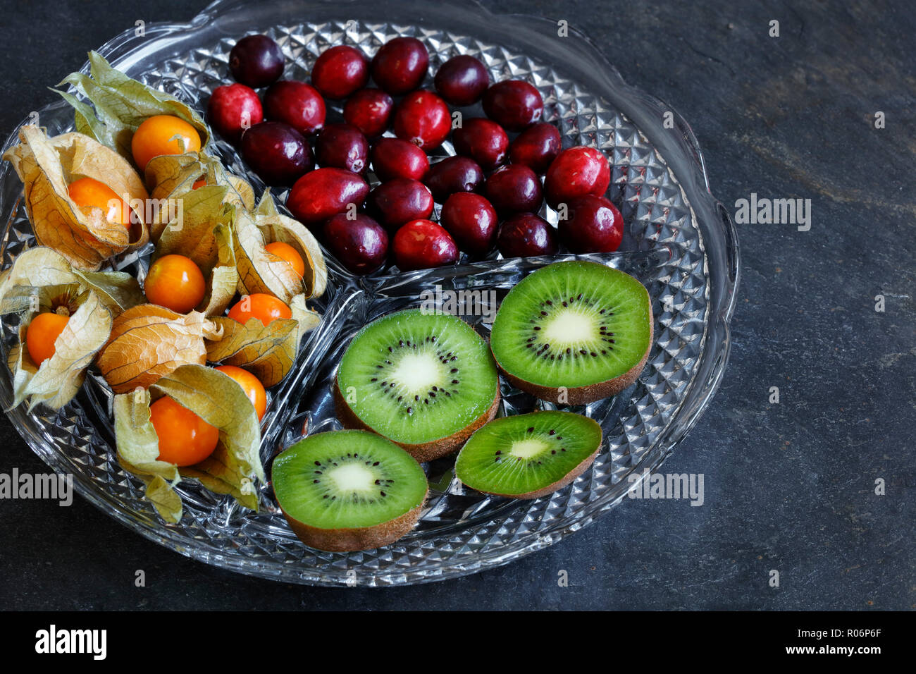 Physalis Früchte - Kap Stachelbeeren mit Preiselbeeren und Kiwi auf Schnitt Glas Platter auf schiefer Hintergrund - mit Kopie Raum Stockfoto