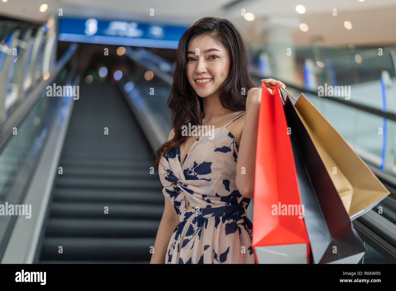 Glückliche junge Frau mit Einkaufstüten auf der Rolltreppe in Mall Stockfoto