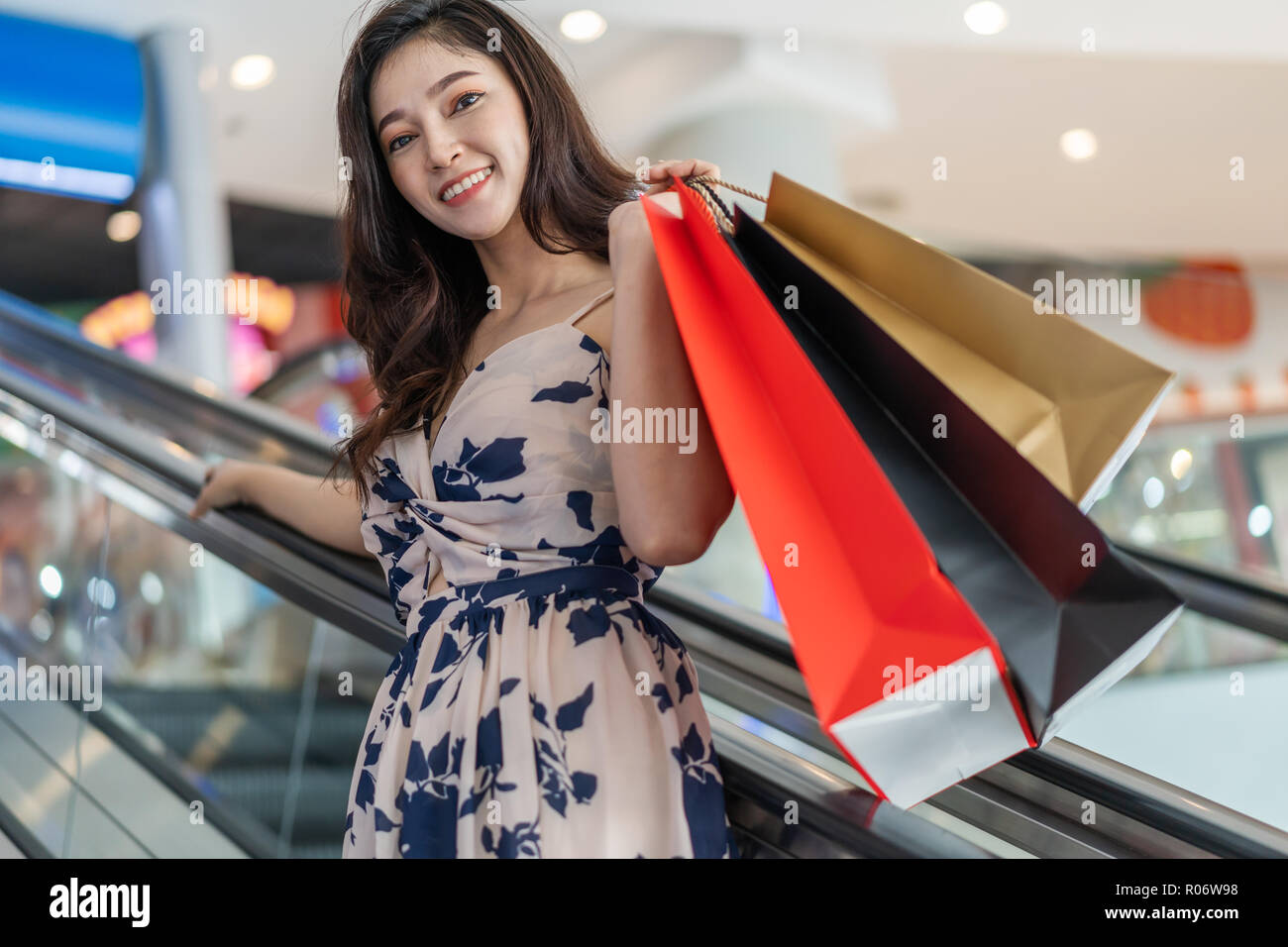 Glückliche junge Frau mit Einkaufstüten auf der Rolltreppe in Mall Stockfoto
