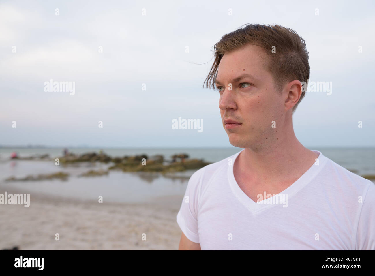 Nahaufnahme von jungen gutaussehenden Mann denken am öffentlichen Strand von H Stockfoto