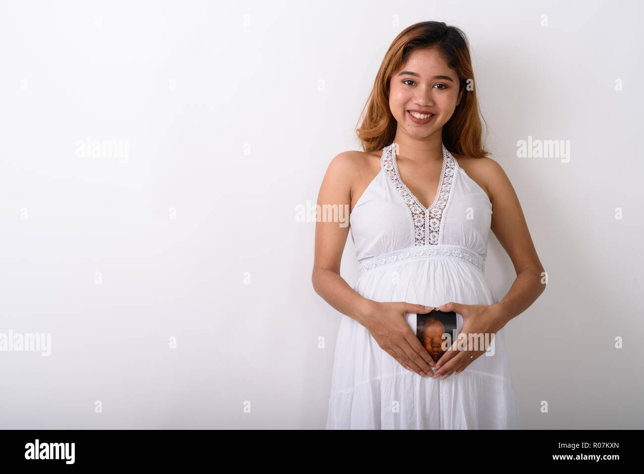 Studio shot von jungen asiatischen schwangere Frau glücklich lächelnd, während Ho Stockfoto