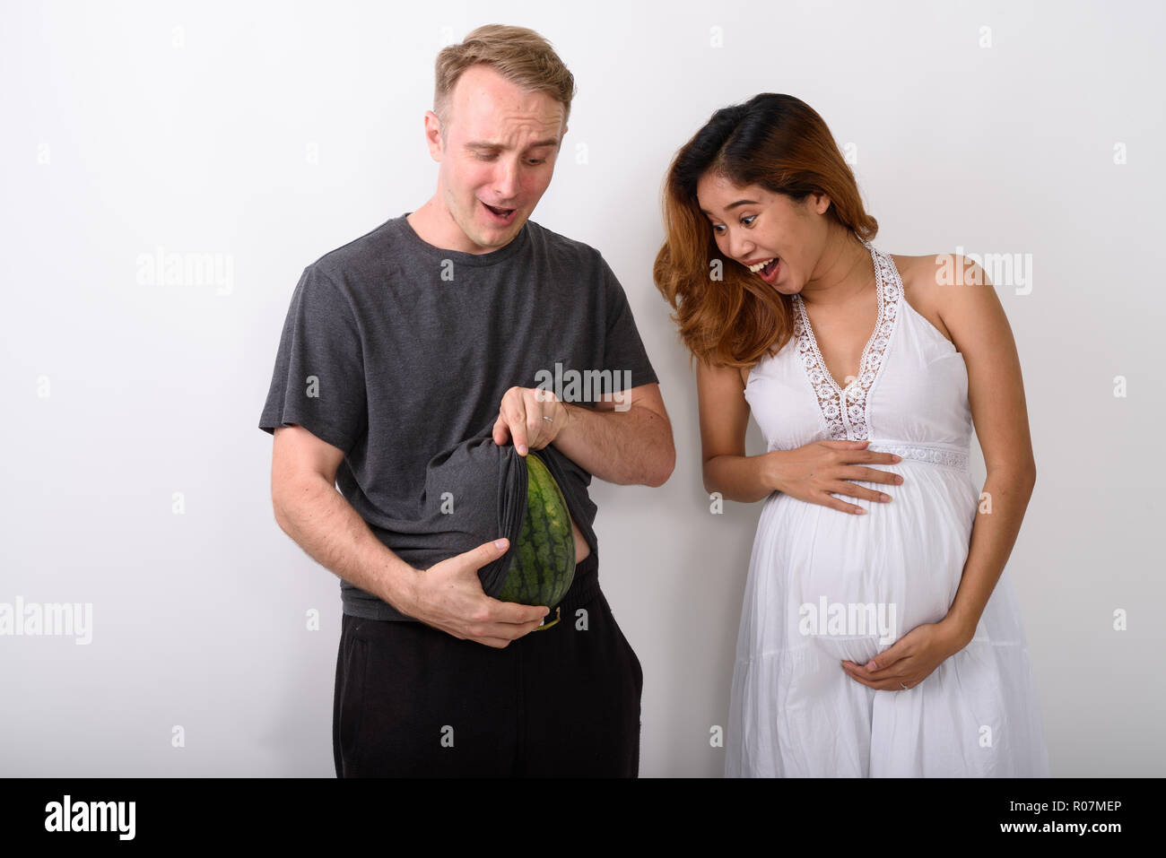 Mann mit seinem Magen wie würde er schwanger mit Wassermelone, während Frau lachend Stockfoto