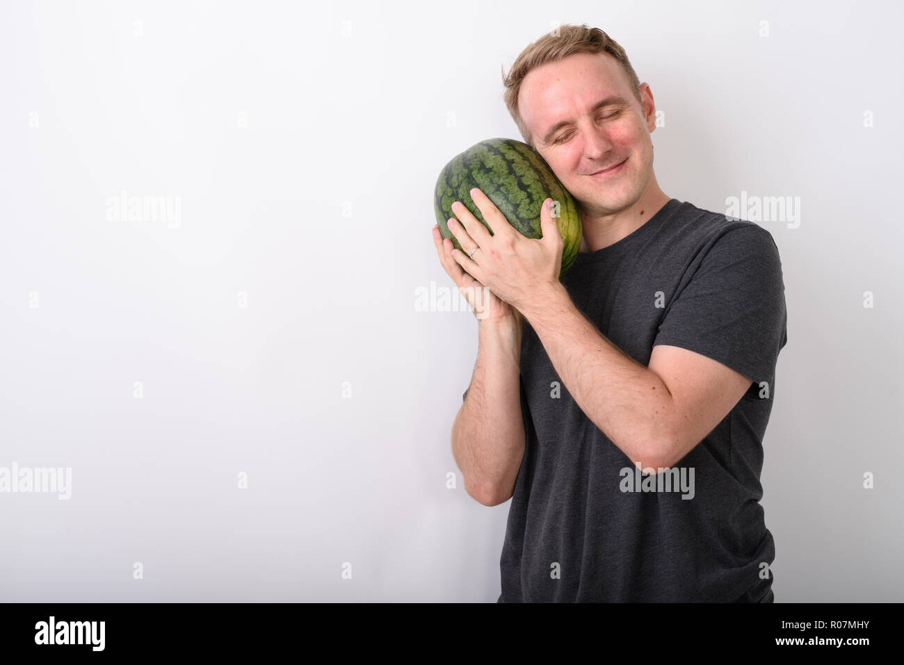 Studio shot Junger stattlicher Mann mit Wassermelone als Baby Witz Stockfoto