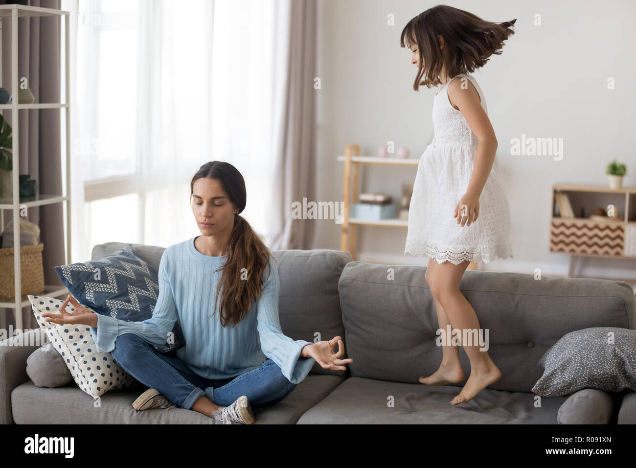 Kleine Mädchen springt auf die couch Mutter Yoga Stockfoto