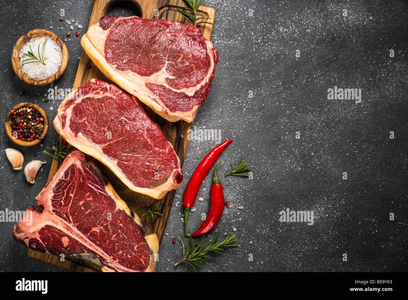 Rohes Fleisch Rindfleisch Steak. Black Angus Prime Fleisch - Ribeye, Roastbeef, T-Bone Steaks auf Schneidebrett. Draufsicht auf Schwarzer Tisch mit kopieren. Stockfoto