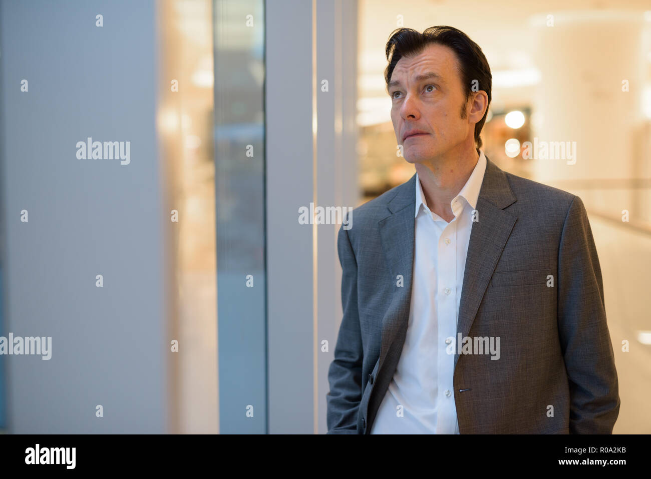 Portrait von Reifen gut aussehender Geschäftsmann auf der Suche durch das Fenster Stockfoto
