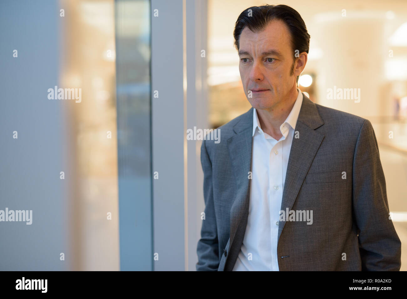 Portrait von Reifen gut aussehender Geschäftsmann auf der Suche durch das Fenster Stockfoto