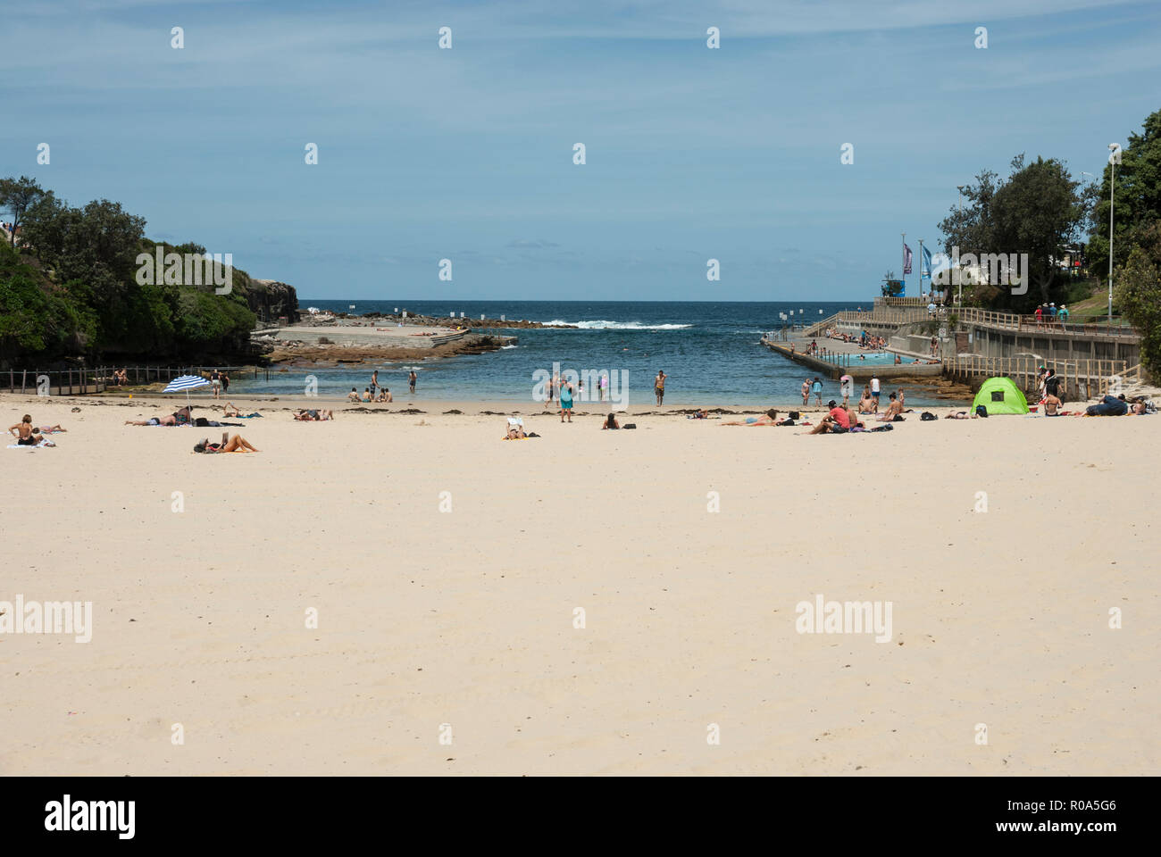 Blick auf den goldenen Sandstrand von Clovelly Beach, Sydney, mit Menschen, mit Sonnenbaden und Schwimmen im Meer und auf der rechten Seite ein Schwimmbad. Stockfoto