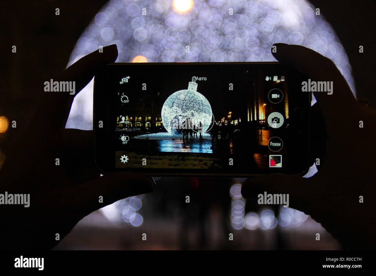Riesige neue Jahr beleuchtete Kugel durch die Kamera des Mobiltelefons in Mädchen Hand in der Nacht. Die Kugel auf den Hintergrund unscharf Stockfoto
