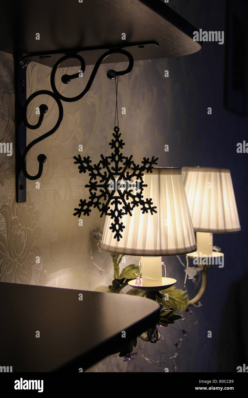 Gemütliche dunkle Inneneinrichtung Weihnachten Neujahr mit kleinen Wall flower Lampe Wandleuchte und Schneeflocke Spielzeug auf Bücherregale closeup Stockfoto